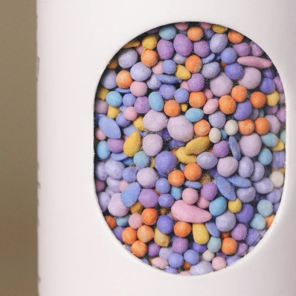 Close-up of colorful coated wildflower seed pellets inside the window of Fleuryx California Bloom Native Wildflower Mix shaker tube, with each pellet color-matched to the flower species it contains.