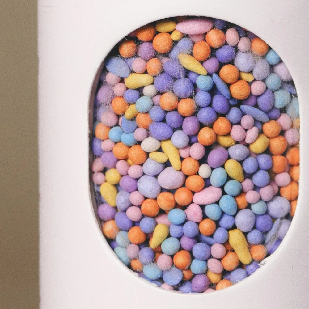 Close-up of colorful coated wildflower seed pellets inside the window of Fleuryx Cascade Bloom Native Wildflower Mix shaker tube, with each pellet color-matched to the flower species it contains.