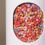 Close-up of colorful coated wildflower seed pellets inside the window of Fleuryx Desert Bloom Native Wildflower Mix shaker tube, with each pellet color-matched to the flower species it contains.