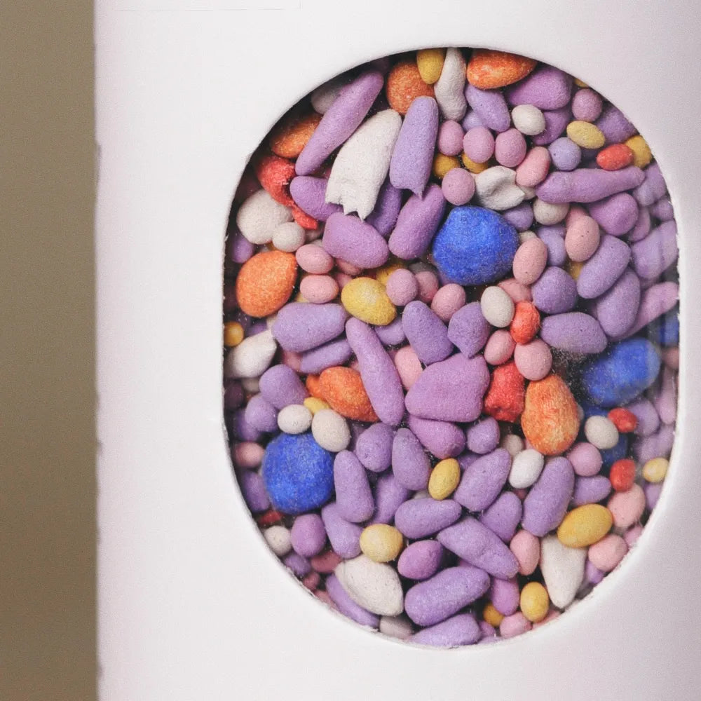 Close-up of colorful coated wildflower seed pellets inside the window of Fleuryx Frontier Bloom Native Wildflower Mix shaker tube, with each pellet color-matched to the flower species it contains.