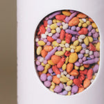 Close-up of colorful coated wildflower seed pellets inside the window of Fleuryx Prairie Bloom Native Wildflower Mix shaker tube, with each pellet color-matched to the flower species it contains.